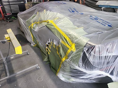 A car is wrapped in plastic and tape in a garage.