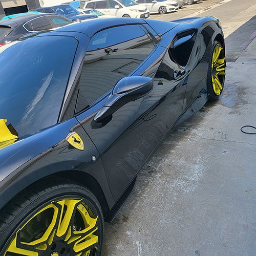 A black sports car with yellow wheels is parked in a parking lot.