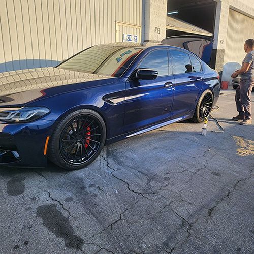 A man is standing next to a blue bmw m5.