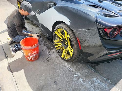 A man is kneeling down next to a black sports car with yellow wheels.