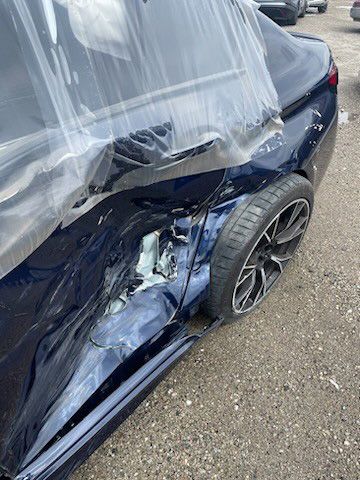 A blue car with a damaged side is wrapped in plastic.