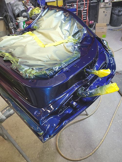 A blue car is being painted in a garage