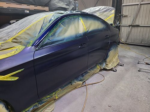 A purple car is being painted in a garage.