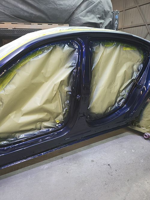 A blue car is being painted in a garage.