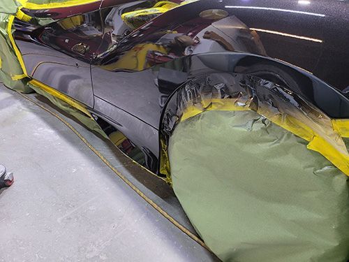 A black car is being painted in a garage.