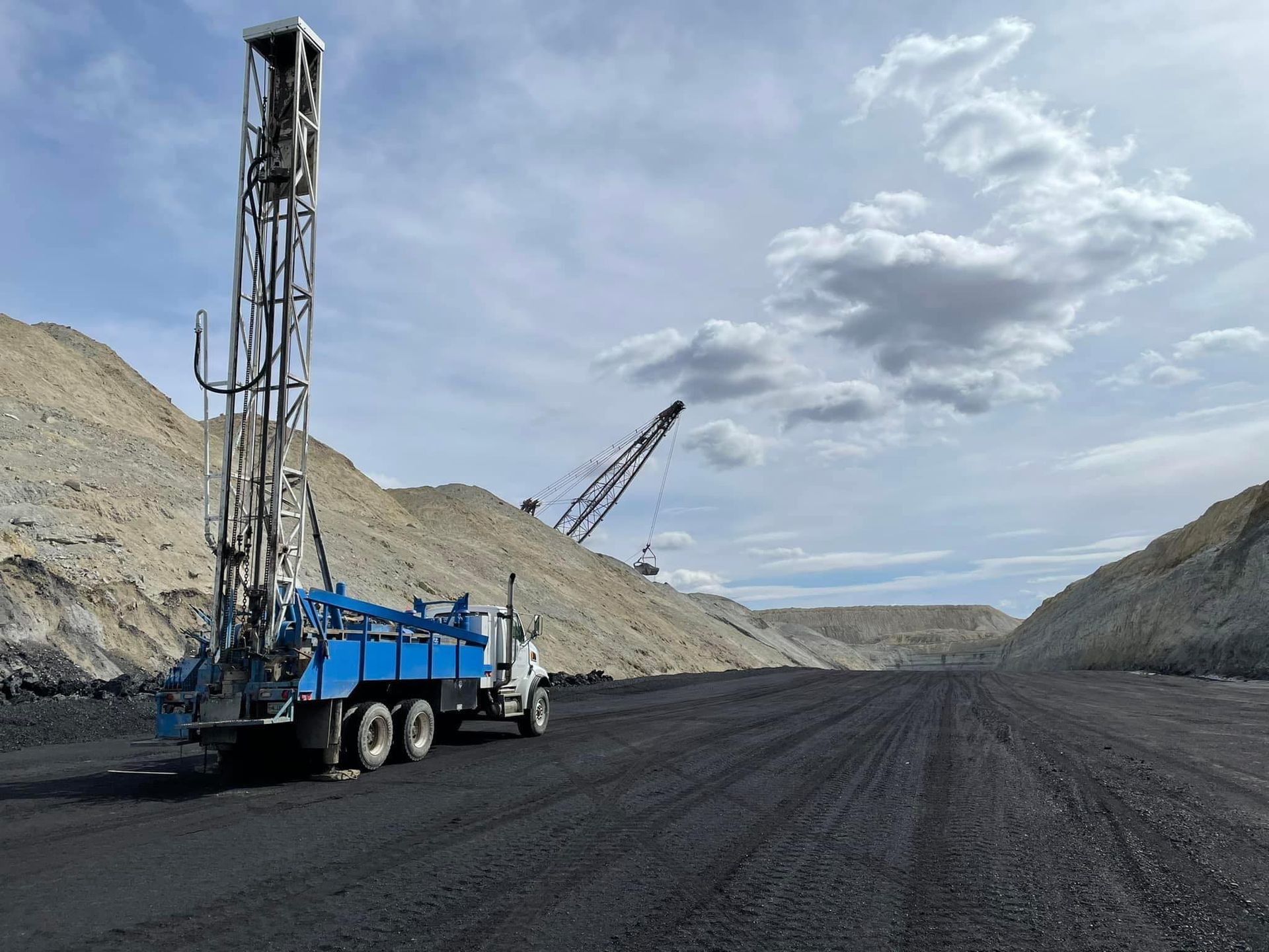 A truck is parked in a dirt field with a crane in the background