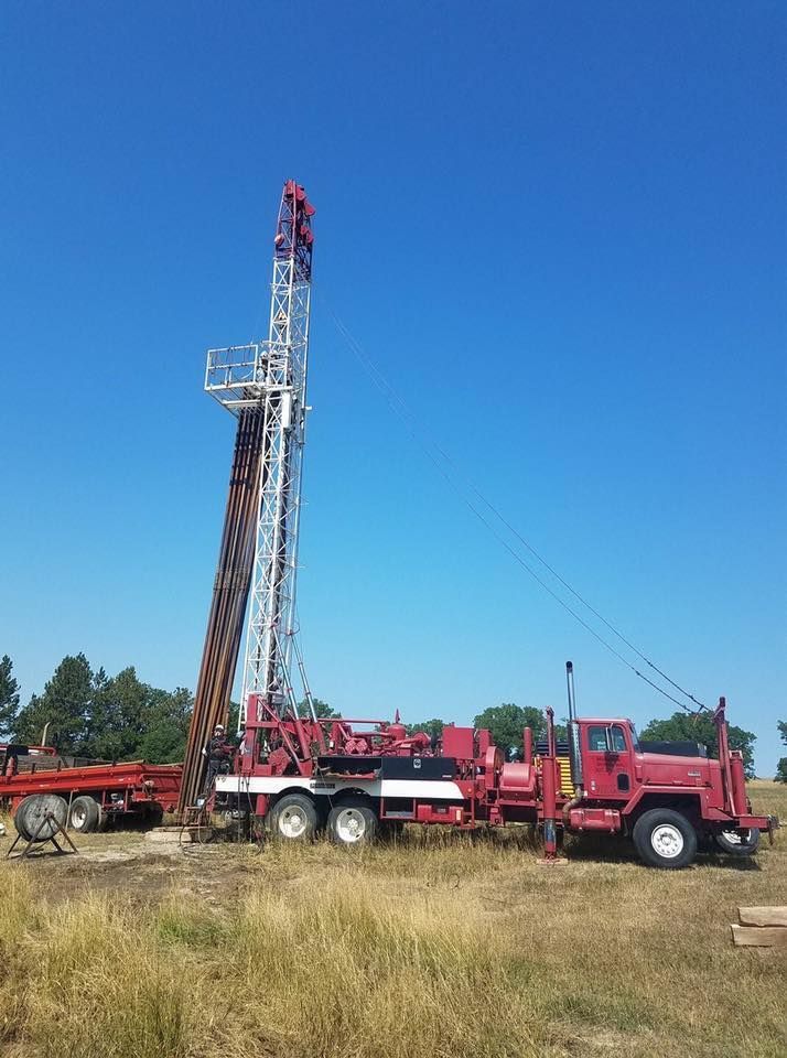 A red truck is parked in a field next to a drilling rig.