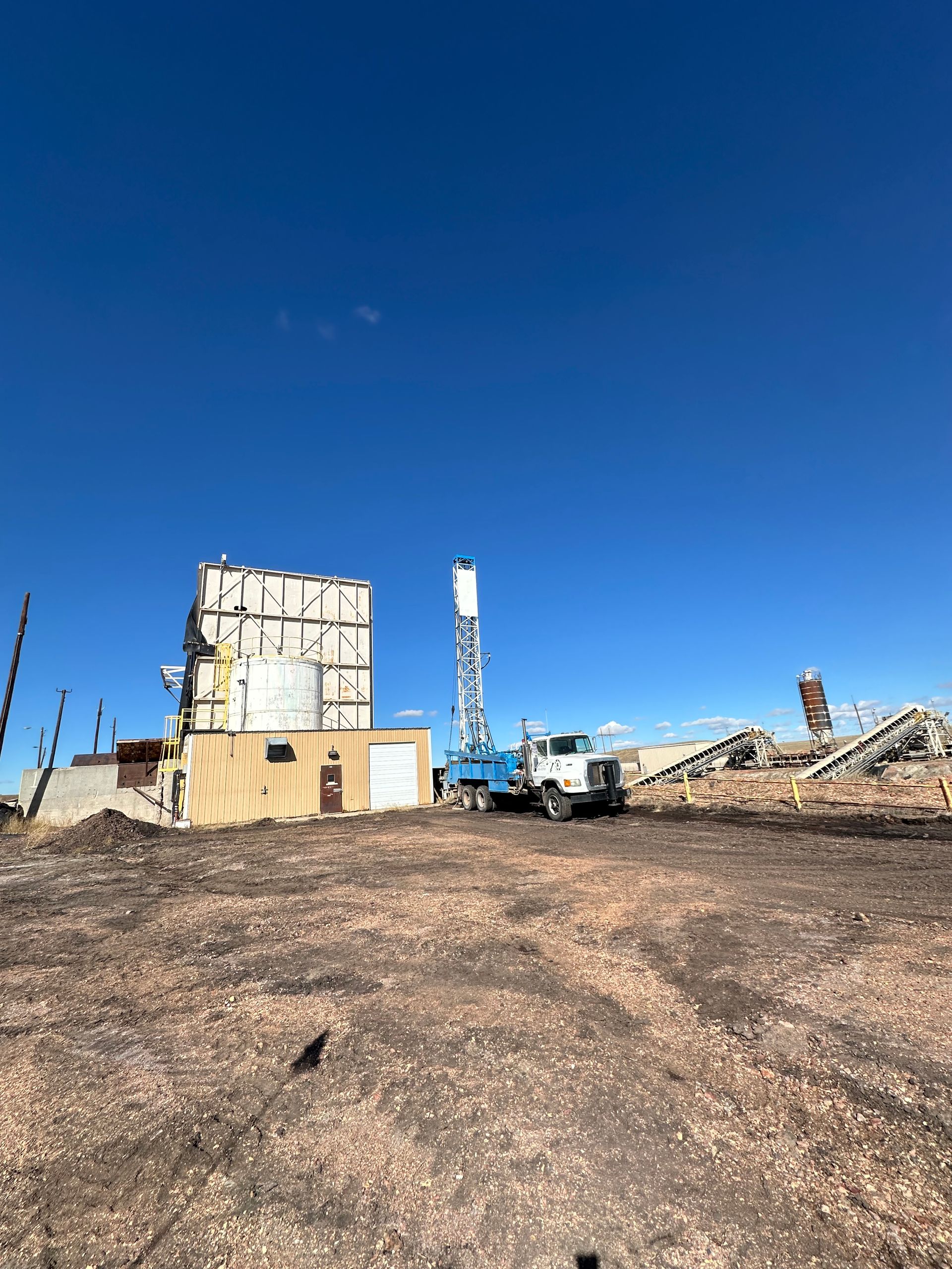 A blue truck is parked in a dirt field in front of a building.