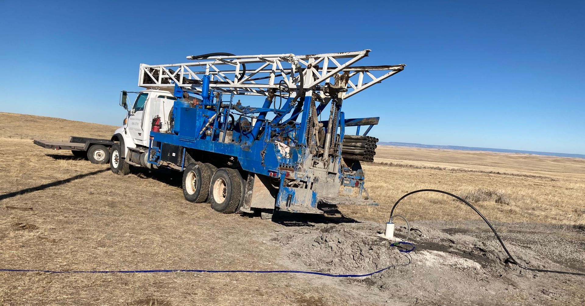 A truck is driving down a dirt road next to a drilling rig.