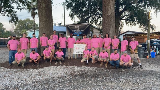 Large group in matching pink shirts posing outdoors beneath trees at a community event