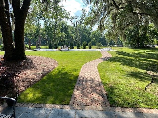 Brick path winding through a sunny green park with trees and a grassy lawn