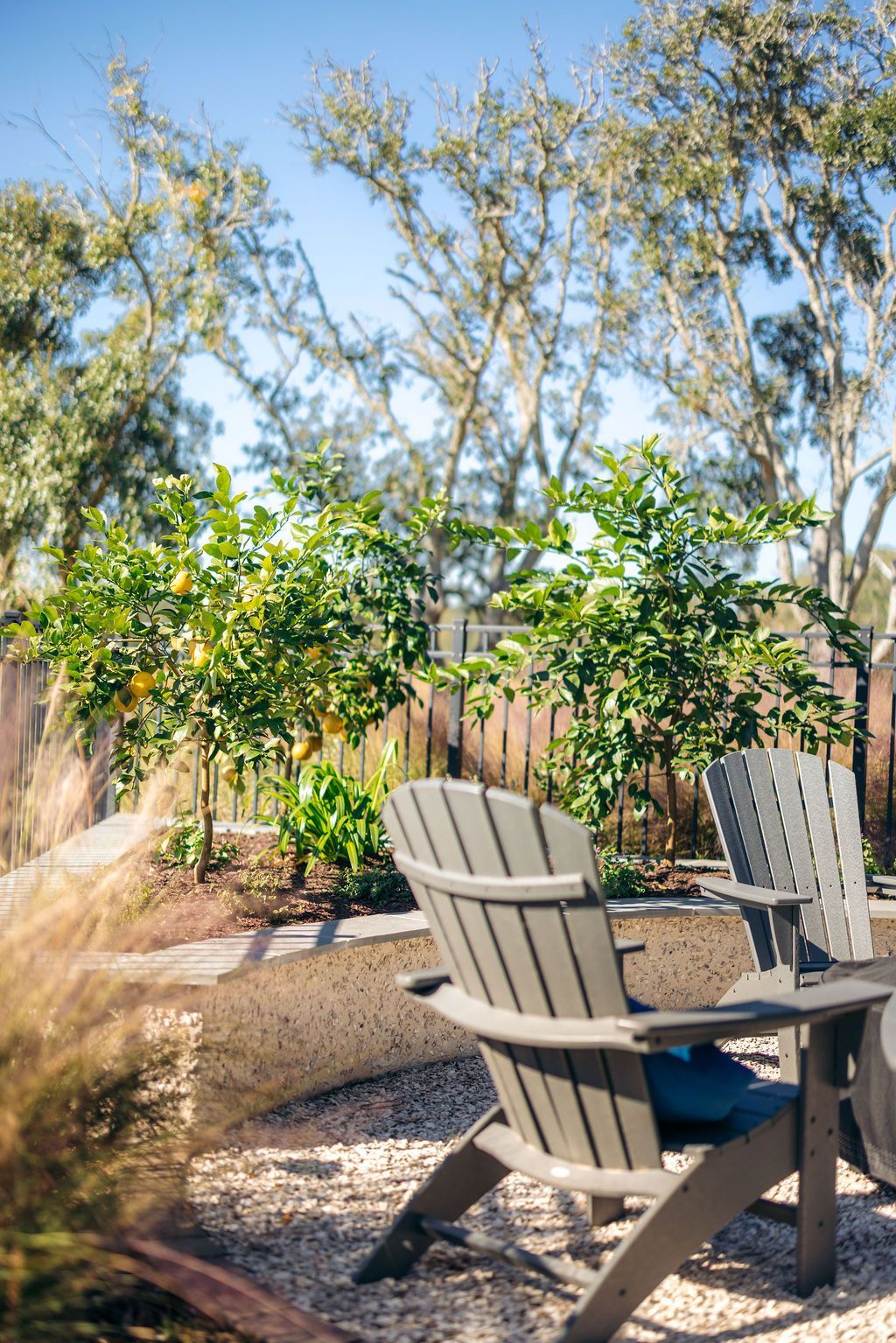 Backyard patio with two wooden chairs, a small table, gravel, and trees in bright sunlight
