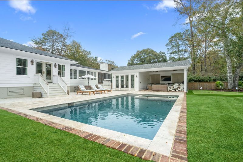Modern white house with a backyard pool, patio seating, and green lawn under a blue sky
