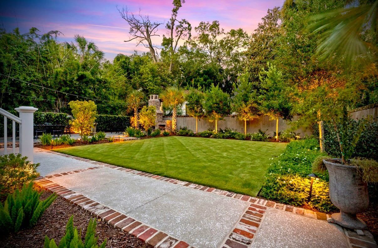 Lush backyard garden with a green lawn, stone path, and trees at sunset