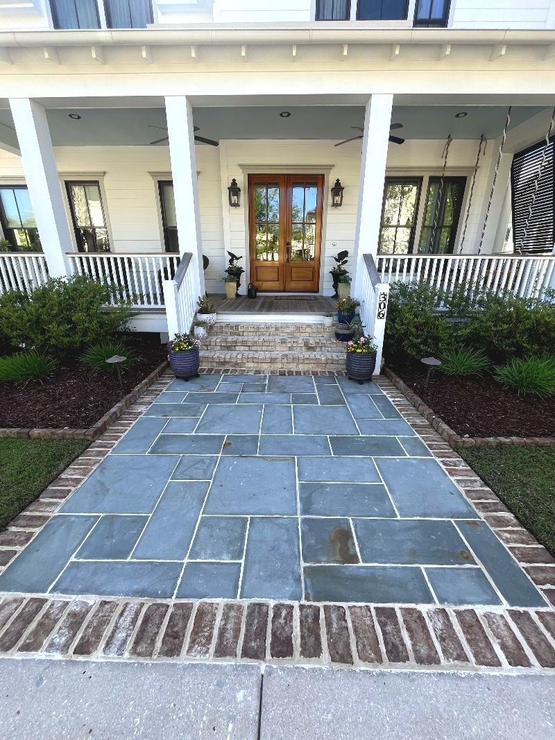 Stone walkway leading to a porch with white railings and a wooden front door