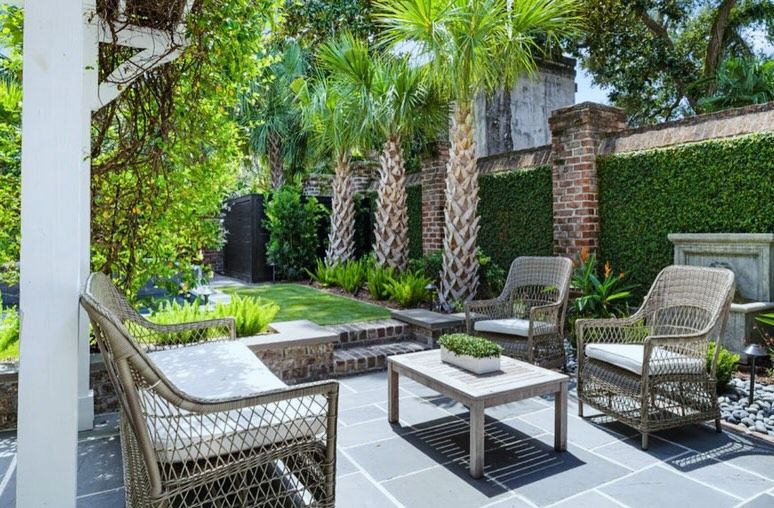 Outdoor patio with wicker chairs and a coffee table, framed by palm trees and brick walls