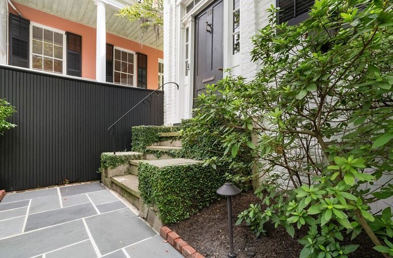Stone patio path beside black fence and ivy-covered steps next to a white house
