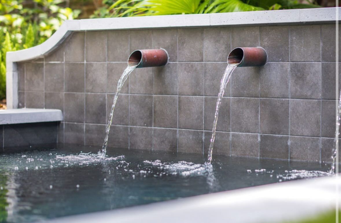 Two copper spouts pour water into a tiled outdoor pool or fountain