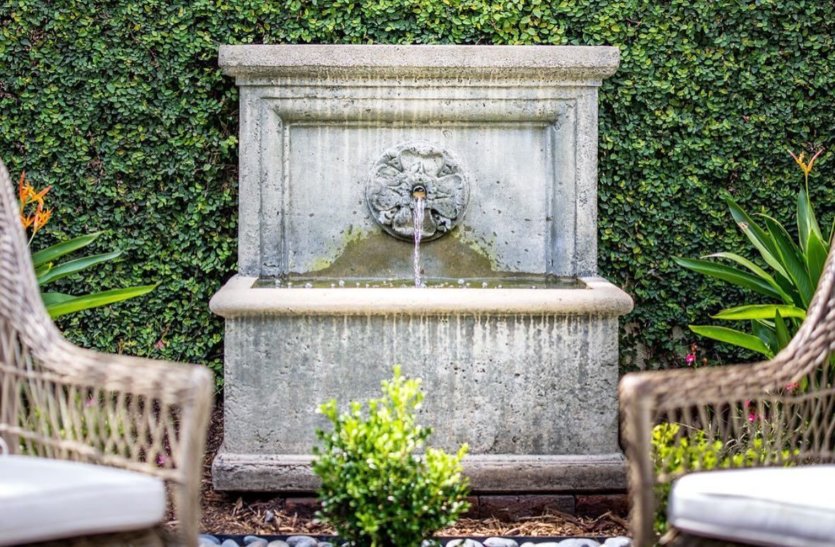 Stone garden fountain with a carved face, framed by ivy and wicker chairs.