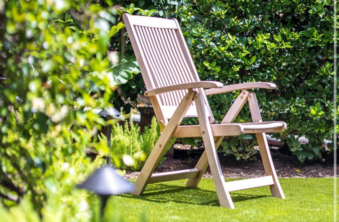 Wooden lounge chair on a sunny lawn with greenery in the background