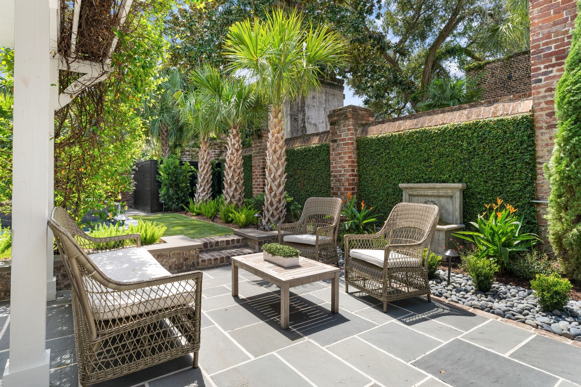 Patio with wicker chairs, coffee table, and lush greenery against brick walls