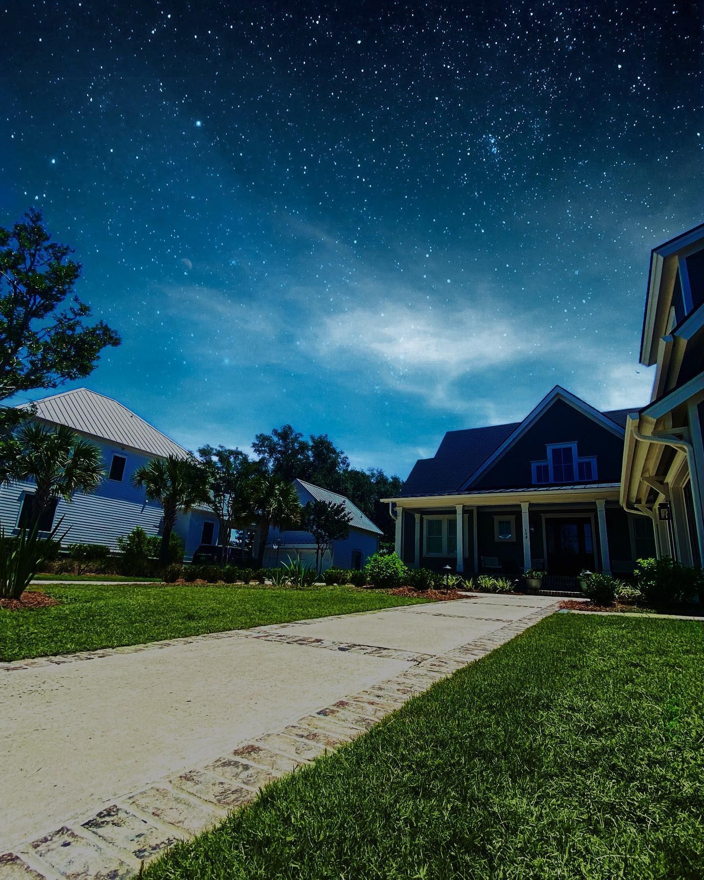 Suburban house at night with a lit walkway, green lawn, and a starry blue sky