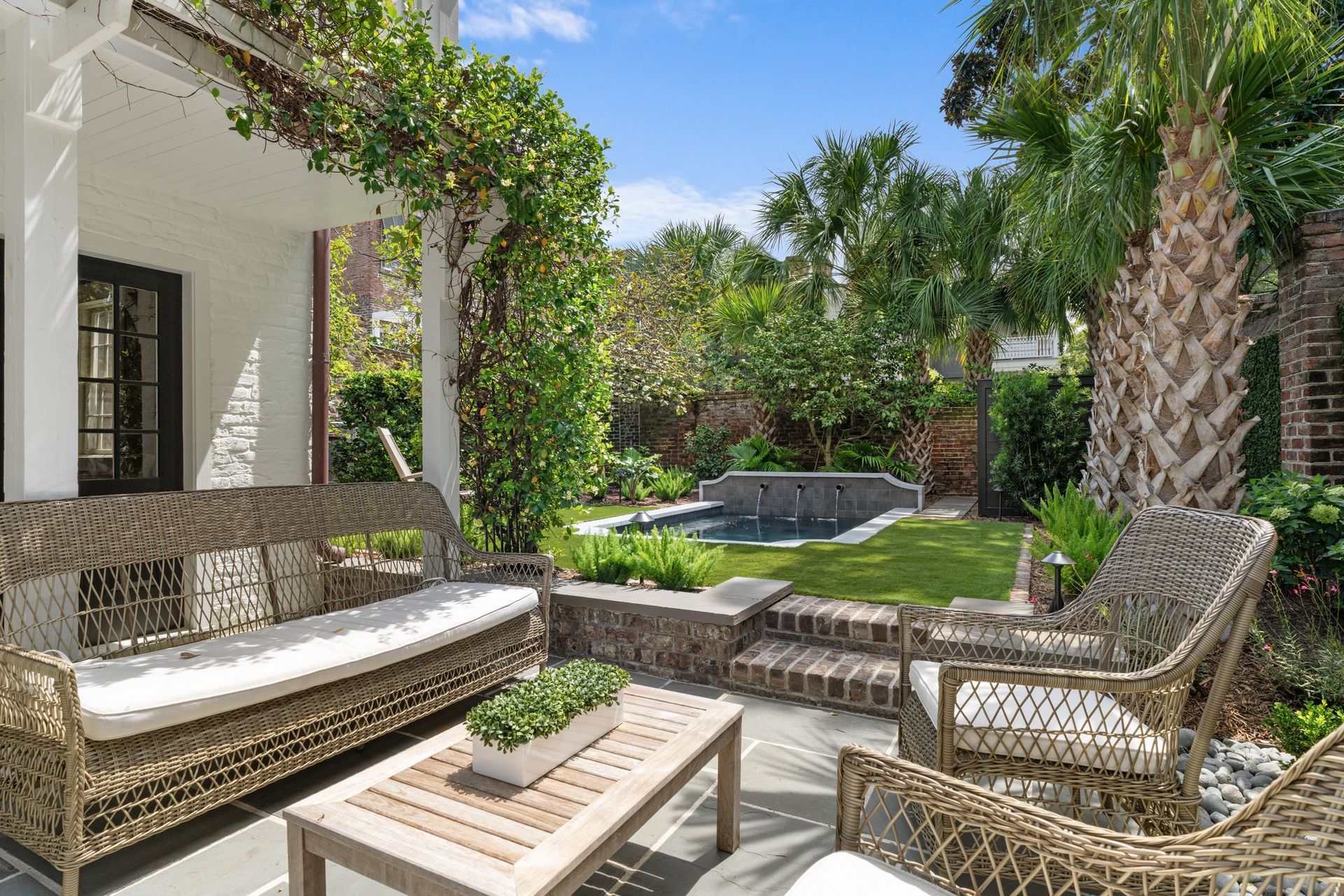 Patio seating area with wicker furniture, a low table, and a green garden in sunlight
