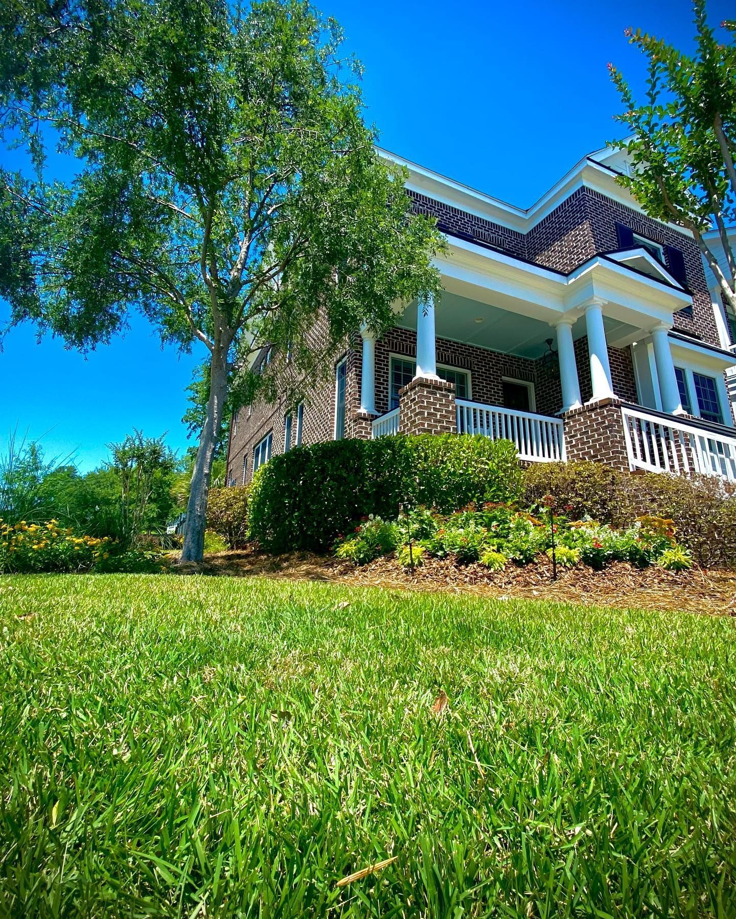 Bright green lawn in front of a white house with a porch under a clear blue sky