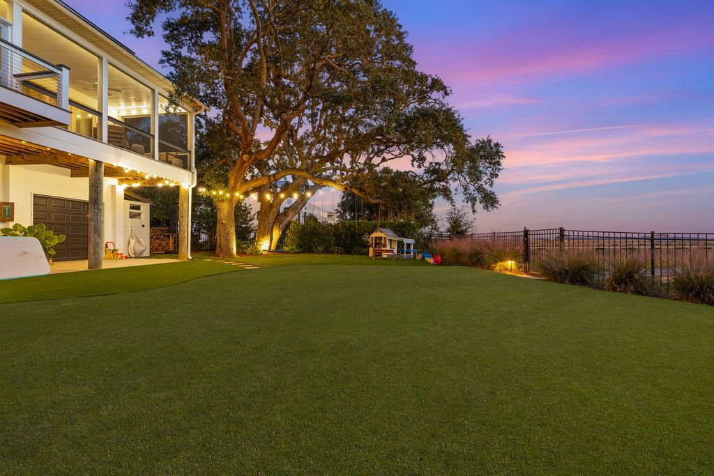 House with lit porch overlooking a large green lawn at sunset with a pink-blue sky