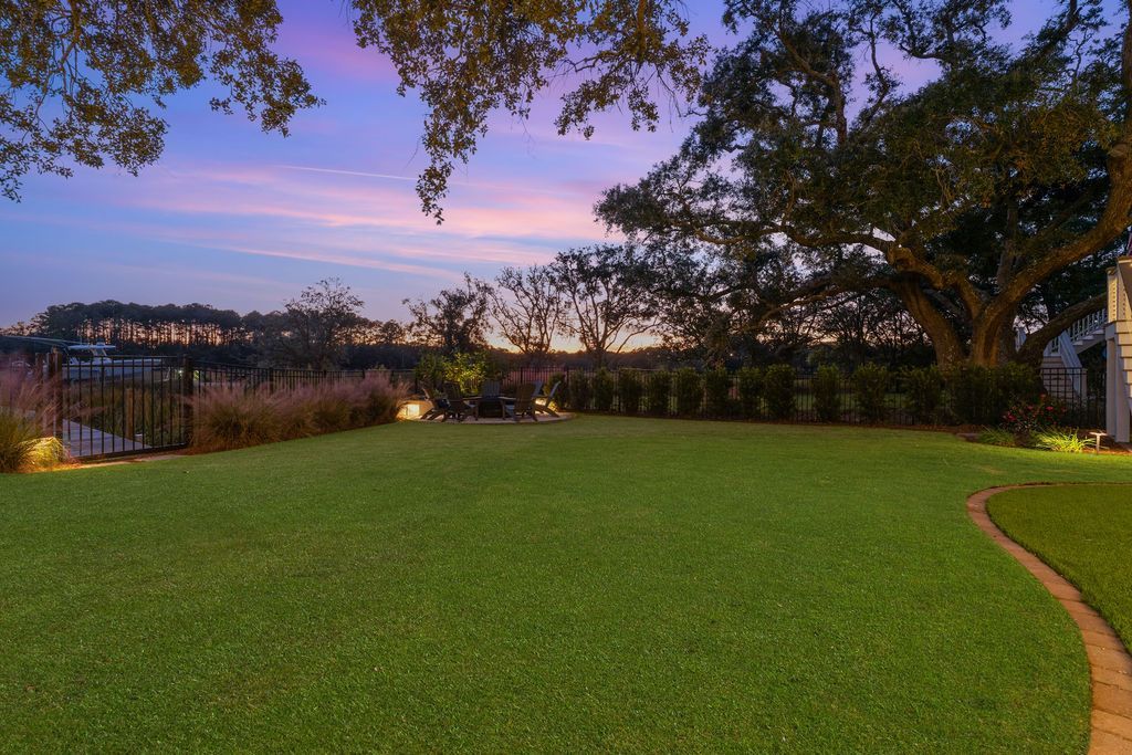 Manicured green lawn at dusk with trees, a pond, and pink-blue sunset sky