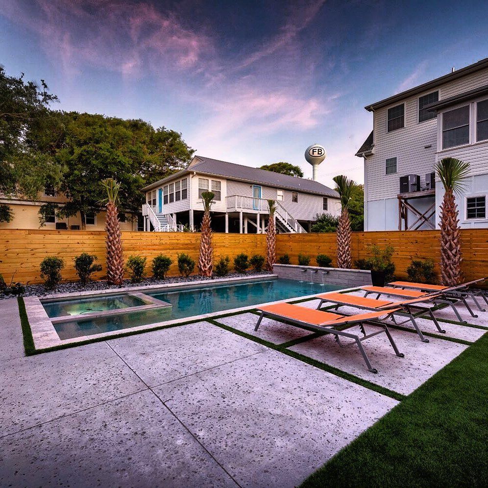 Modern backyard pool with lounge chairs, palm trees, and white house at sunset
