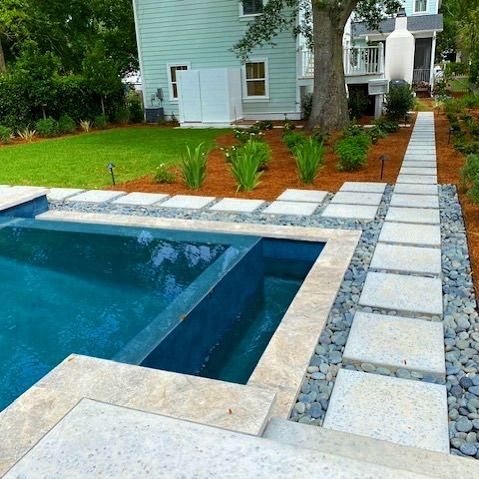 Backyard pool with stone pavers, green lawn, and house in the background