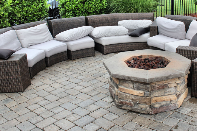 Curved wicker patio seating around a stone fire pit on a paved backyard patio
