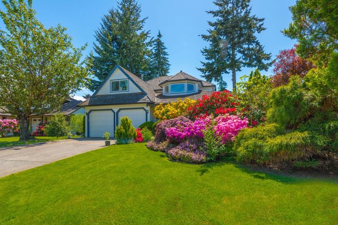 Colorful suburban house with a green lawn and blooming pink and purple garden under a bright blue sky