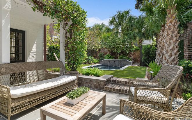 Outdoor patio with wicker seating, low table, and lush garden around a pool on a sunny day