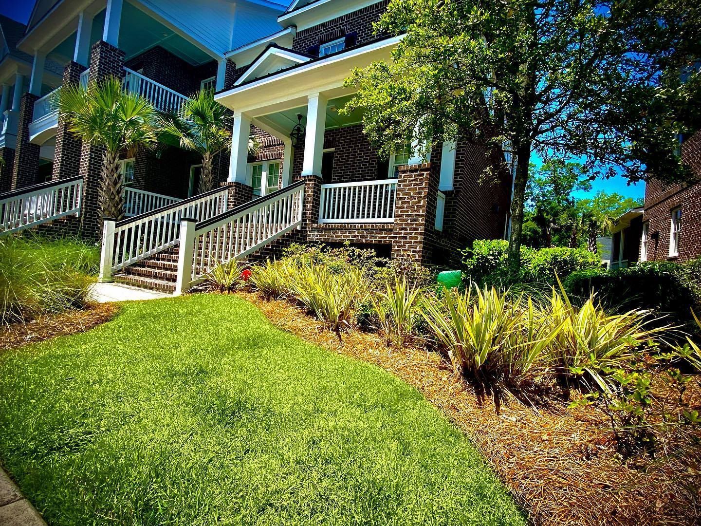 House with white porch and railing above a green lawn, surrounded by trees and shrubs on a sunny day