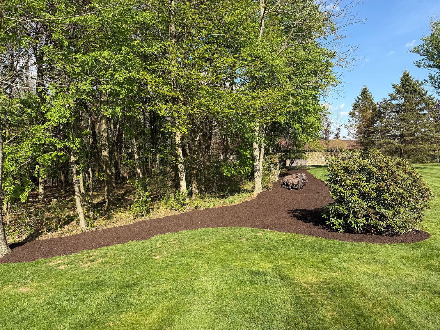 Landscaped backyard with green lawn, trees, mulch beds, and a patio table near a house