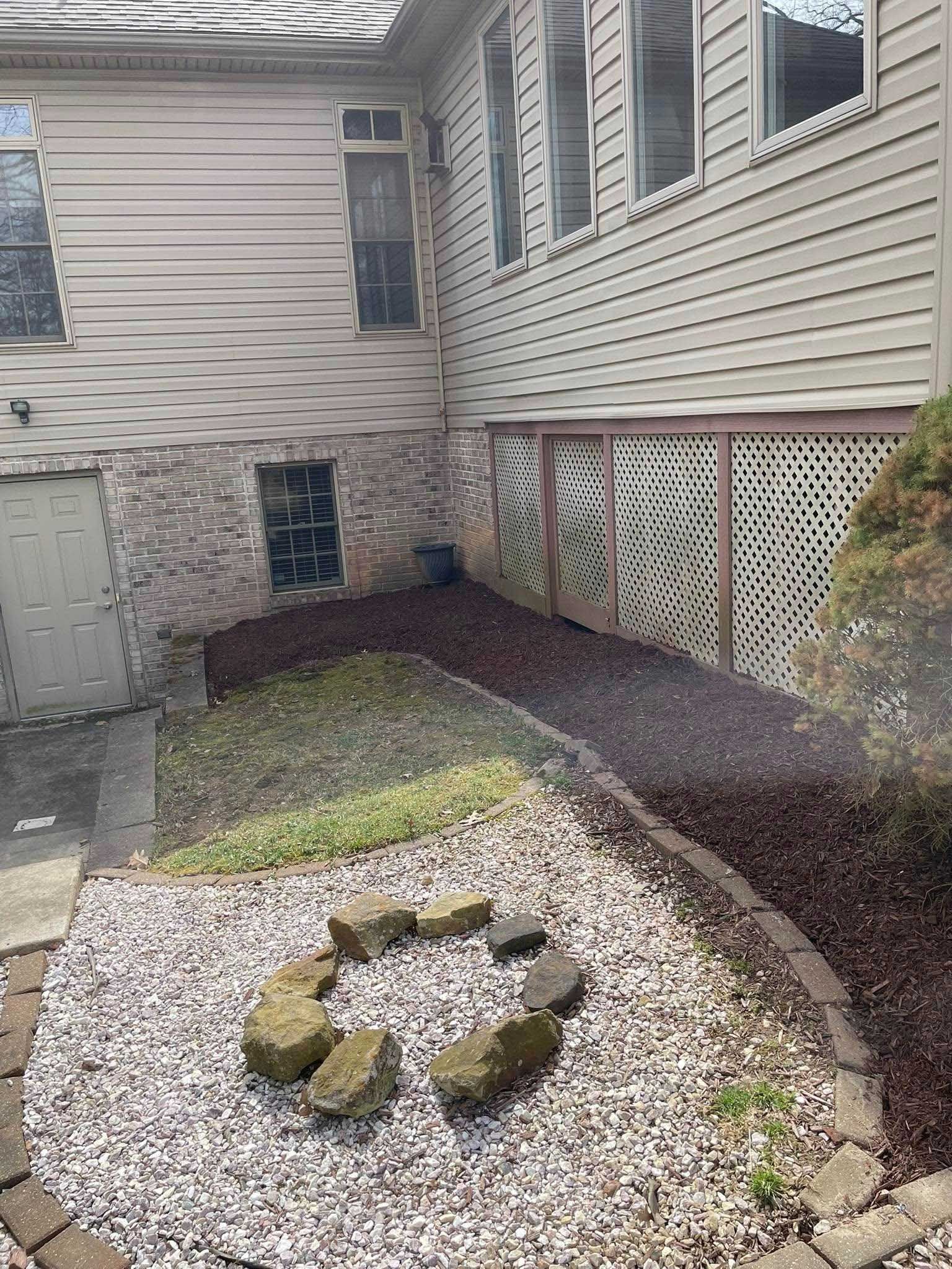Backyard view with a gravel area framing a fire pit, a mulch pathway, and a house with windows.