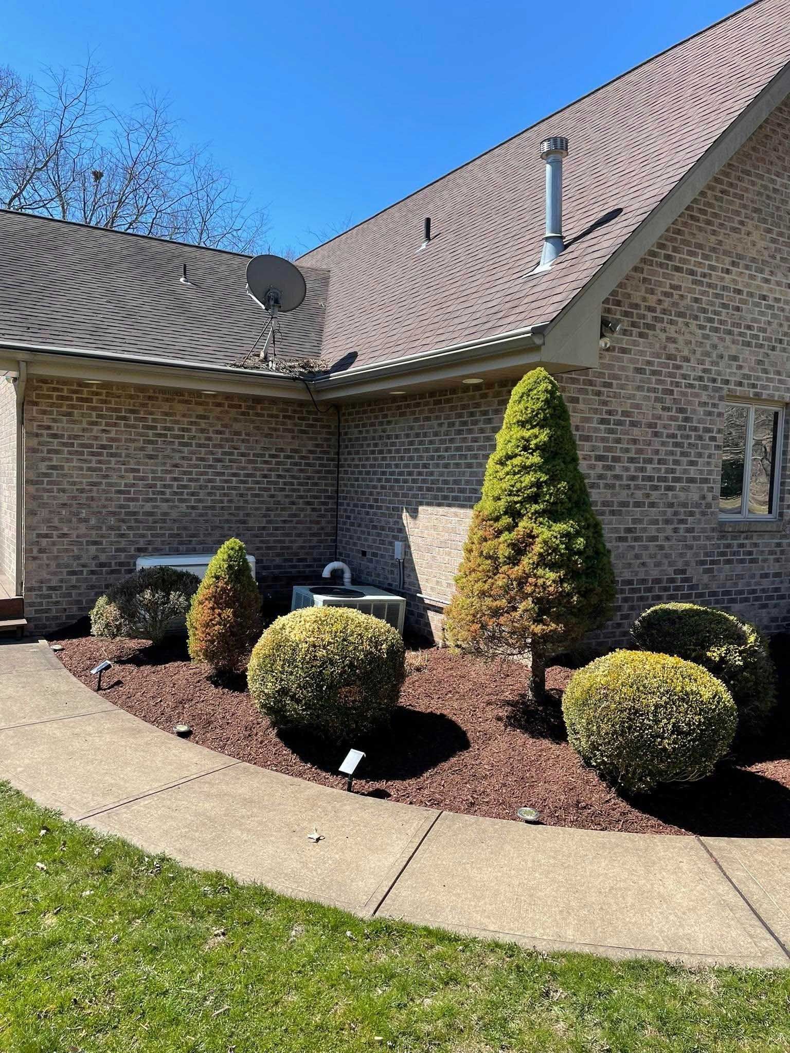 A brick home with a curved walkway and landscaped flowerbed with mulch and shrubs; green grass in the foreground.