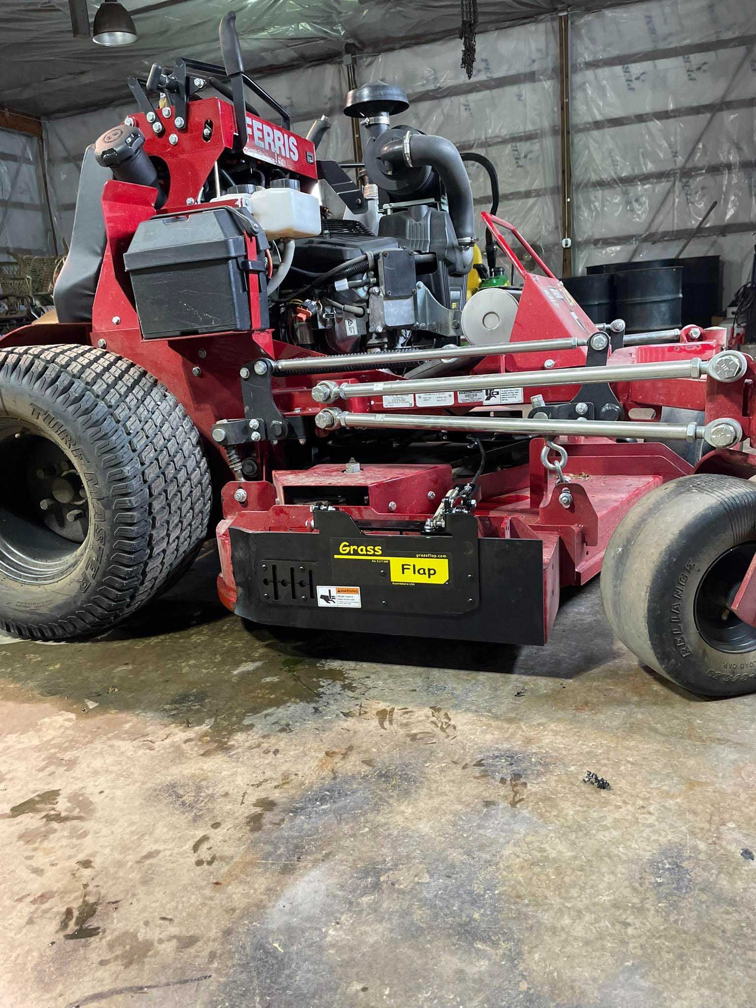 Red commercial lawn mower parked indoors. It is dirty with black tires.