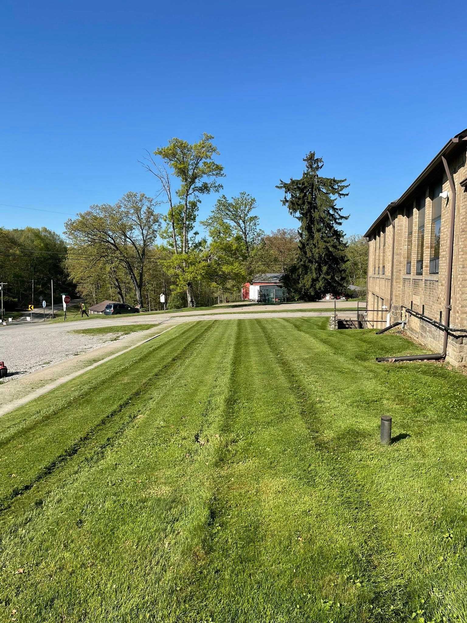 Freshly mowed green lawn with stripes next to a brick building. Trees and a blue sky in the background.