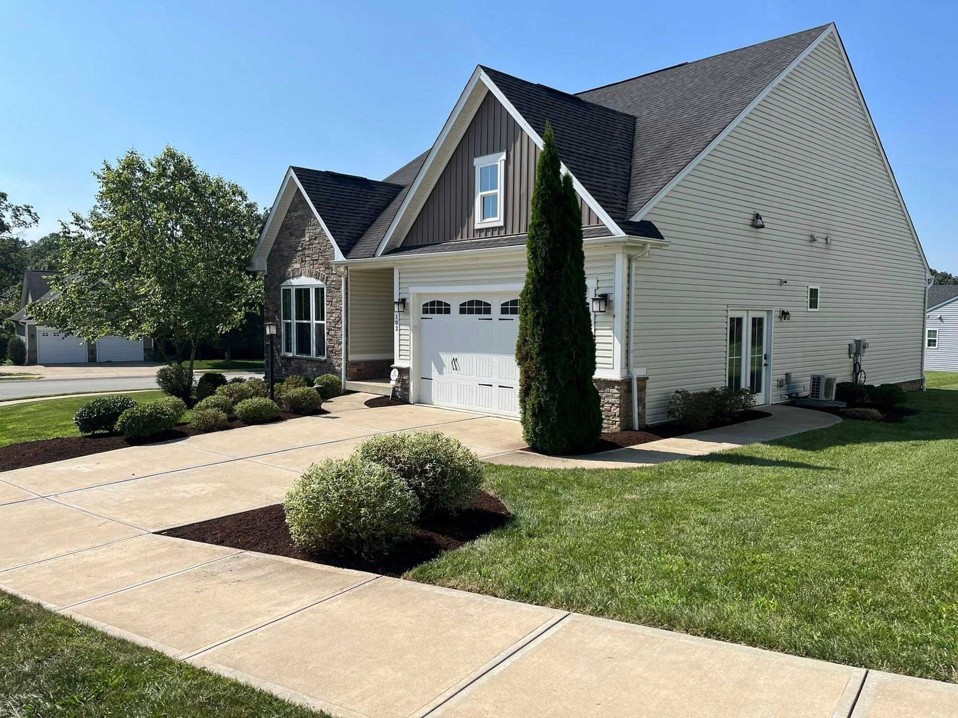 A light-colored house with a driveway and well-manicured lawn under a clear blue sky. The house has a stone facade.