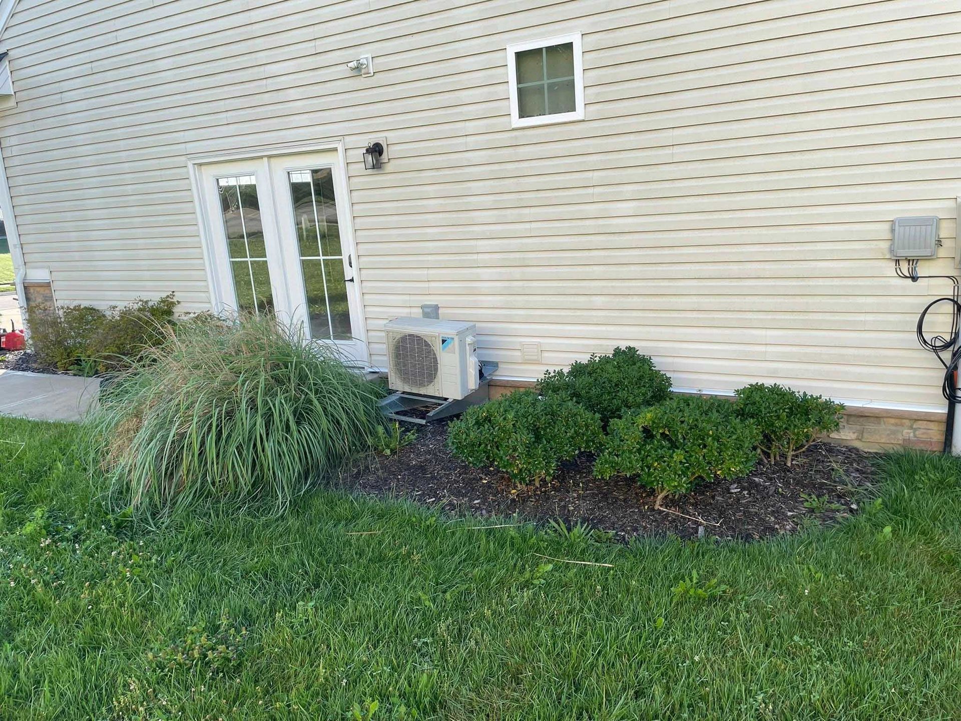 A house exterior with a grassy yard, a small garden bed, a door, and an air conditioning unit.