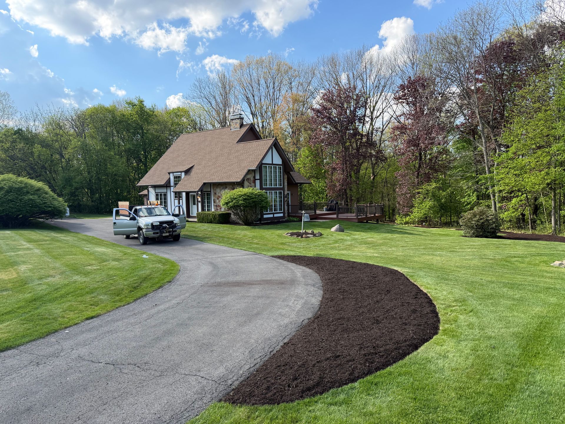 Curved gravel driveway leading to a cottage-style house with a parked pickup truck and landscaped lawn.
