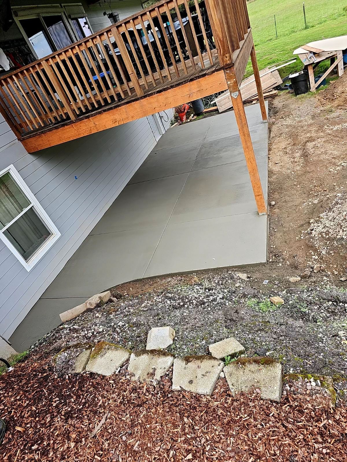 A concrete patio with a wooden deck is being built next to a house.