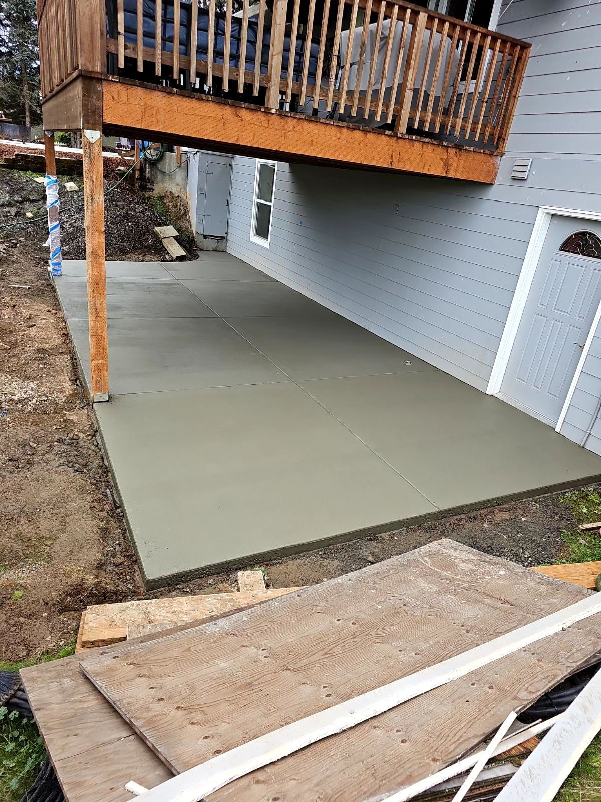 A concrete patio under a deck is being built next to a house.