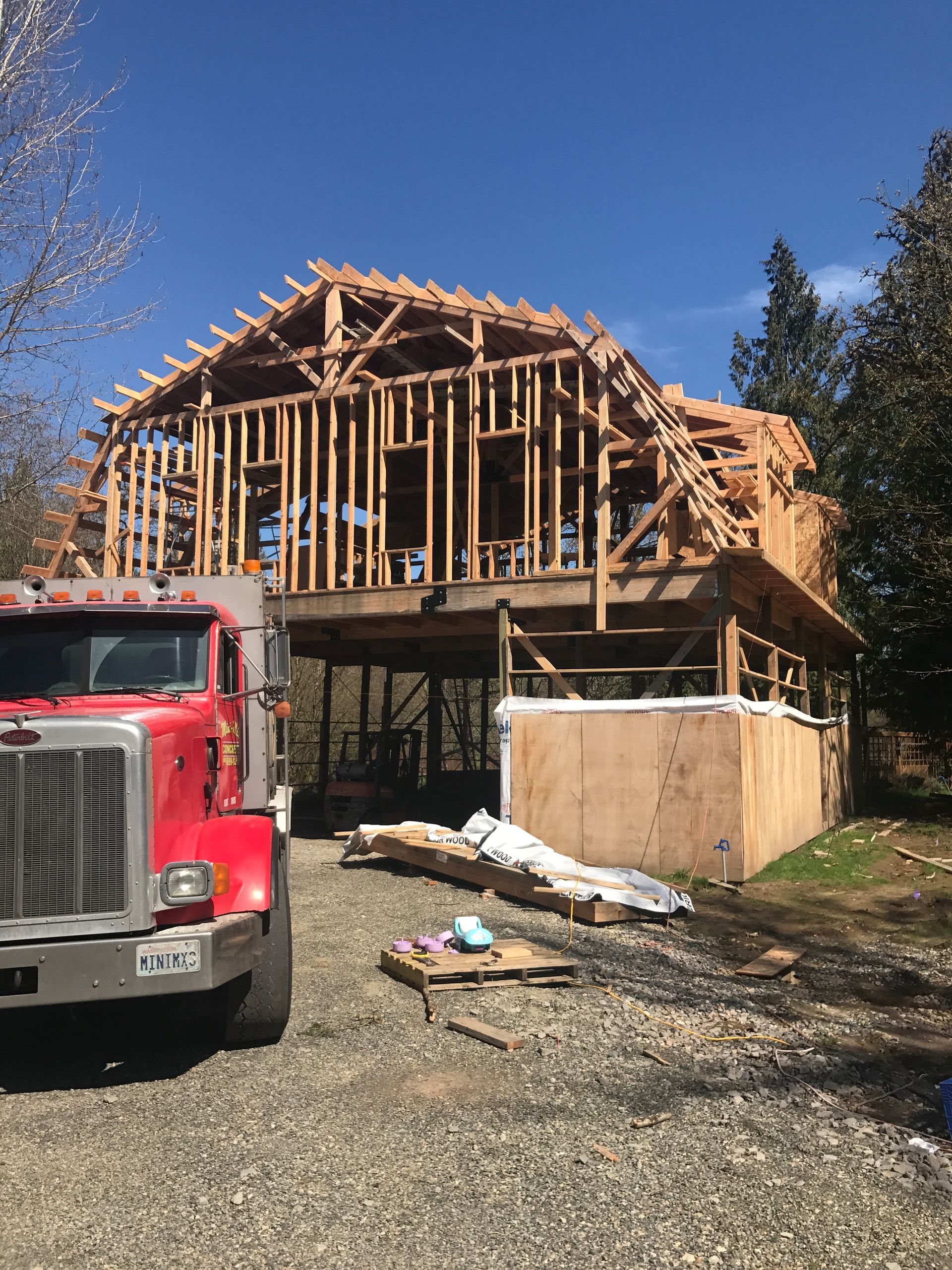 A red semi truck is parked in front of a house under construction.