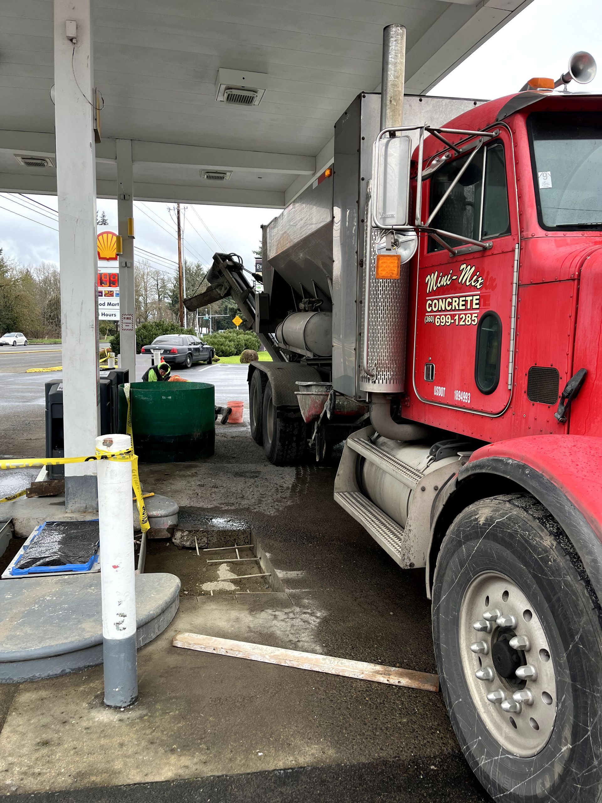 A red truck is parked under a canopy at a gas station.