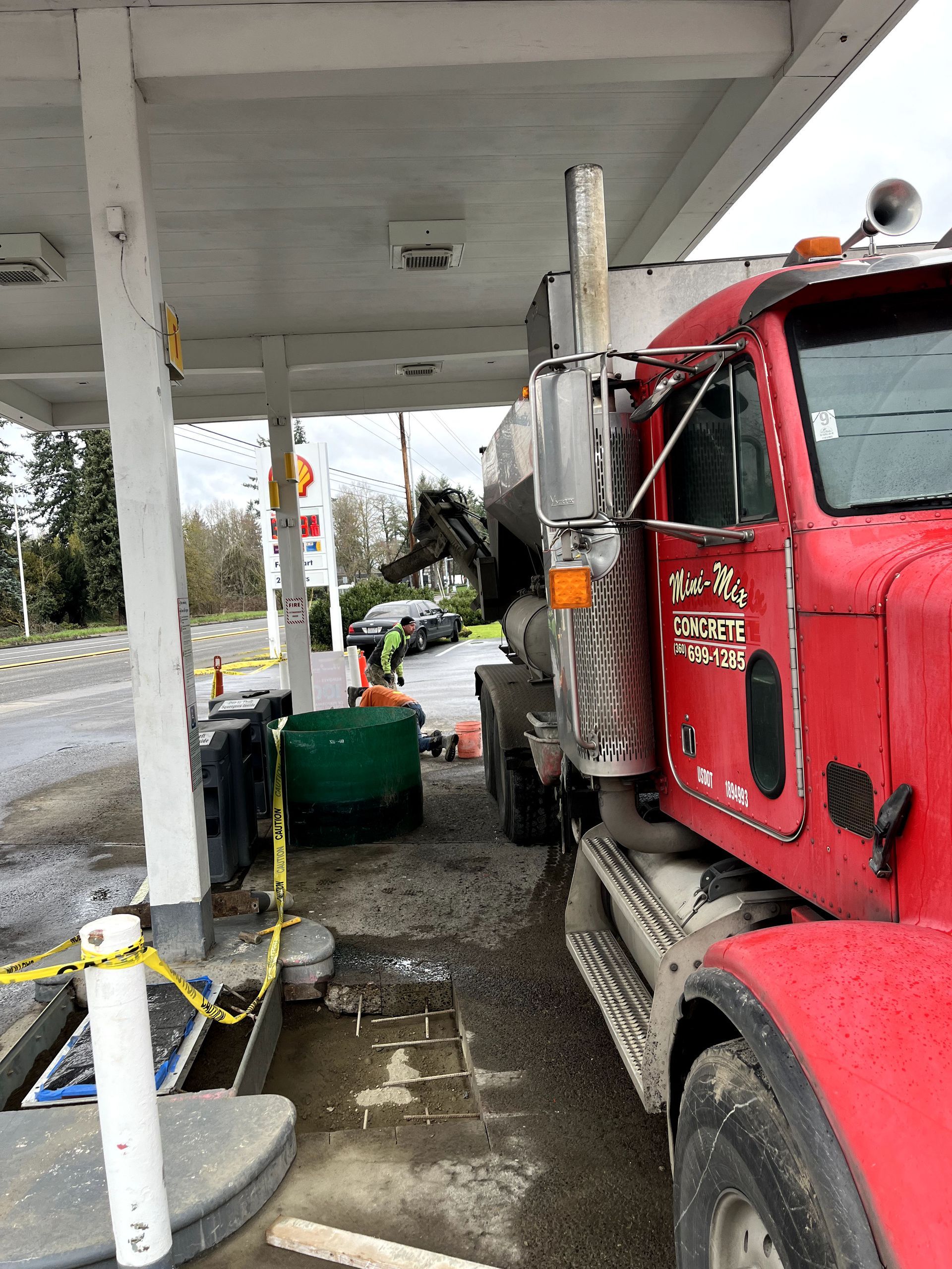 A red truck is parked under a canopy at a gas station.