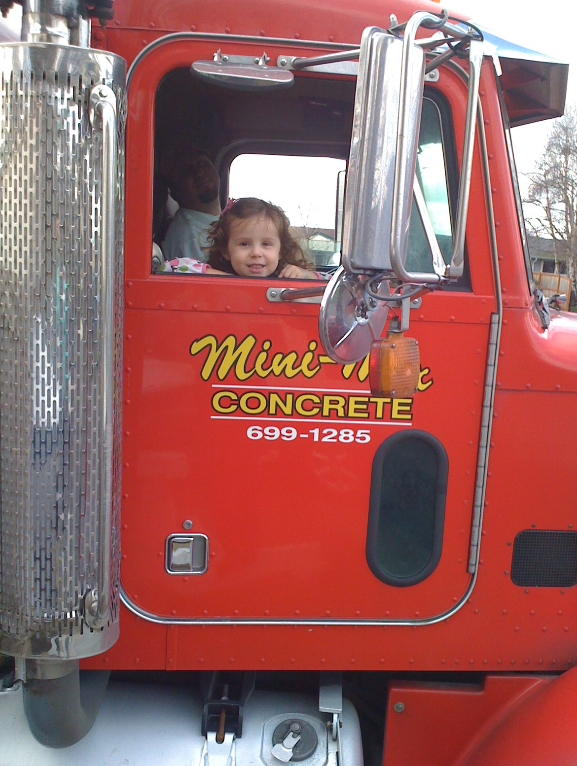 A little girl is looking out the window of a mini concrete truck